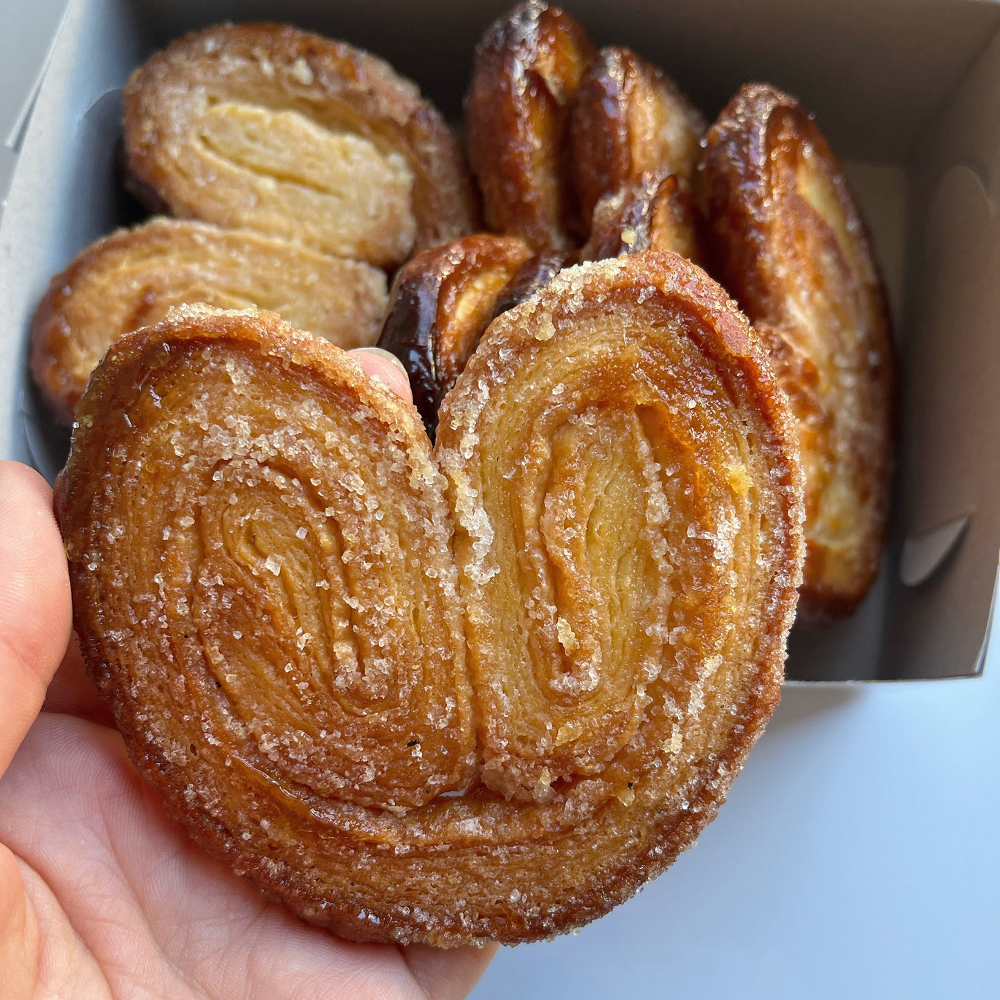 Hand holding a palmier cookie with more of them in a box in the background